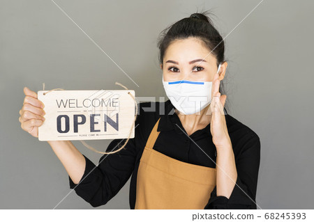 Young Small business owner wore medical face mask,brown apron and the sign for the reopening of the place after the quarantine, invite visit cafe 68245393