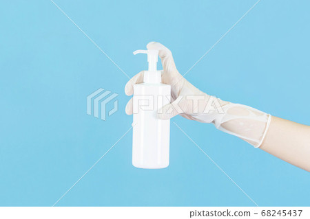 White latex medical gloves on a woman's hand,holding a spay killed the disease or alcohol bottle outstretched isolated on blue background 68245437