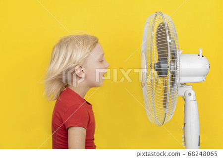Cute blond child enjoying cold air from fan. Cute blond child enjoying cold air from fan. 68248065
