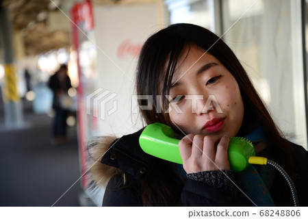 A woman calling with a public phone at the station 68248806