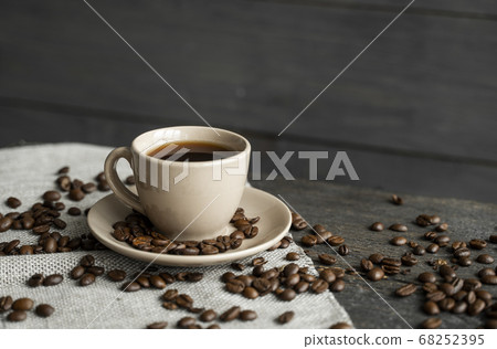 Coffee cup with roasted coffee beans on wooden table background. Mug of black coffe with scattered coffee beans on a wooden table. Fresh coffee beans. Coffee cup with roasted coffee beans on wooden table background. Mug of black coffe with scattered coffee beans on a wooden table. Fresh coffee beans. 68252395