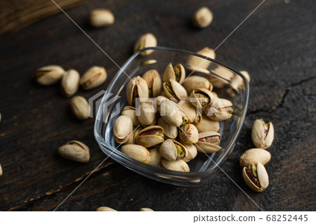 Pistachios in a small plate with scattered nuts of almonds around a plate on a vintage wooden table as a background. Pistachio is a healthy vegetarian protein nutritious food. Natural nuts snacks. Pistachios in a small plate with scattered nuts of almonds around a plate on a vintage wooden table as a background. Pistachio is a healthy vegetarian protein nutritious food. Natural nuts snacks. 68252445