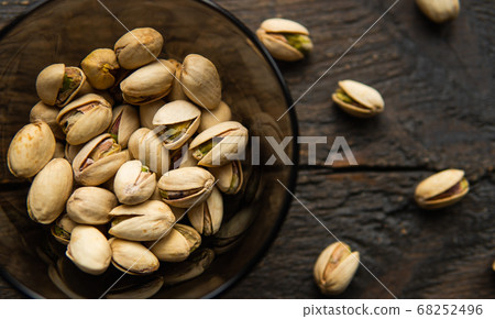 Pistachios in a small plate with scattered nuts of almonds around a plate on a vintage wooden table as a background. Pistachio is a healthy vegetarian protein nutritious food. Natural nuts snacks. Pistachios in a small plate with scattered nuts of almonds around a plate on a vintage wooden table as a background. Pistachio is a healthy vegetarian protein nutritious food. Natural nuts snacks. 68252496