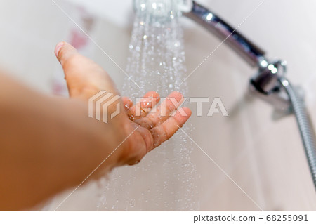 hands check the temperature of the shower water. a man's hand under a stream of water selective focus 68255091