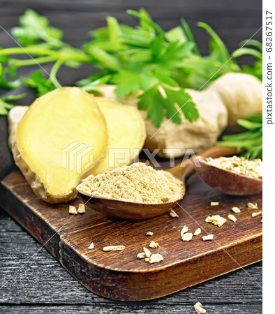 Ginger ground and flakes in spoons on black wood 68267517
