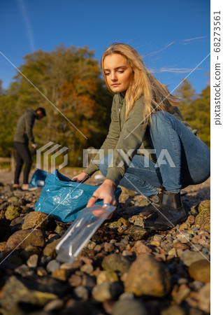 Serious young woman picking up plastic at rocky beach 68273561