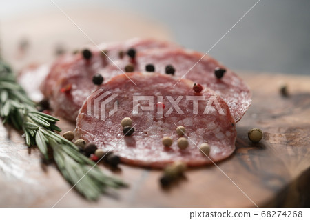 Sliced salame milano sausage on olive wood board with rosemary and pepper 68274268