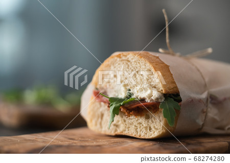 Ciabatta sandwich with salame, arugula, red pesto and cream cheese wrapped in paper on olive board 68274280