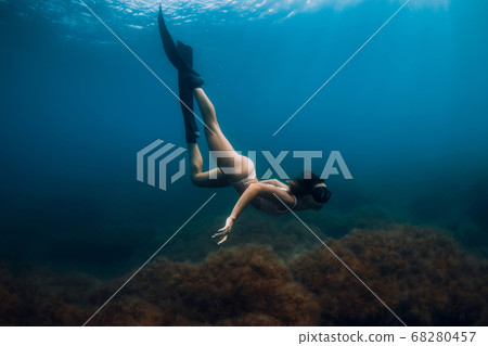 Sporty woman freediver with fins glides underwater in blue sea. Freediving in ocean Sporty woman freediver with fins glides underwater in blue sea. Freediving in ocean 68280457