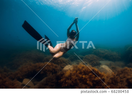 Sporty woman freediver with fins glides underwater in blue sea. Freediving in ocean Sporty woman freediver with fins glides underwater in blue sea. Freediving in ocean 68280458