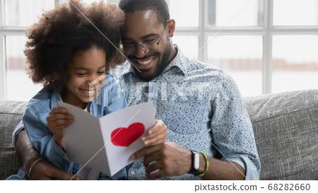 Smiling young biracial dad and daughter read postcard together Smiling young biracial dad and daughter read postcard together 68282660