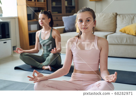 Pretty active teenager in pink tracksuit meditating with mother in living-room 68282971