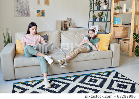 Pretty teenager in headphones and her serious mother in casualwear using gadgets Pretty teenager in headphones and her serious mother in casualwear using gadgets 68282996