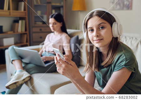 Pretty teenage girl with blond hair holding smartphone while choosing music 68283002
