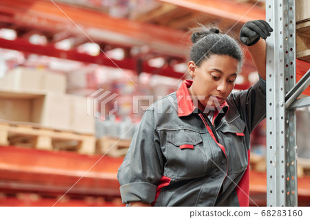 Young tired mixed-race female in uniform and gloves leaning against rack Young tired mixed-race female in uniform and gloves leaning against rack 68283160