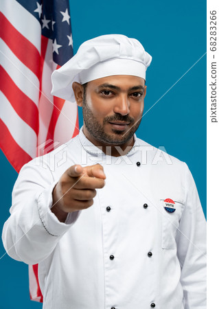 Serious male chef of restaurant with vote insignia on chest pointing at you 68283266