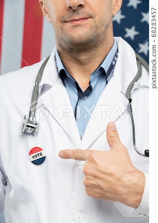 Hand of contemporary mature American clinician in whitecoat pointing at insignia 68283457