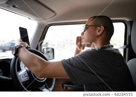 A man looking at a smartphone while driving 68284555