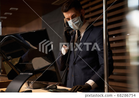 Professional receptionist in medical mask receiving phone calls Professional receptionist in medical mask receiving phone calls 68286754