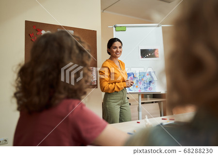 Happy pretty woman enjoying art lesson with pupils Happy pretty woman enjoying art lesson with pupils 68288230
