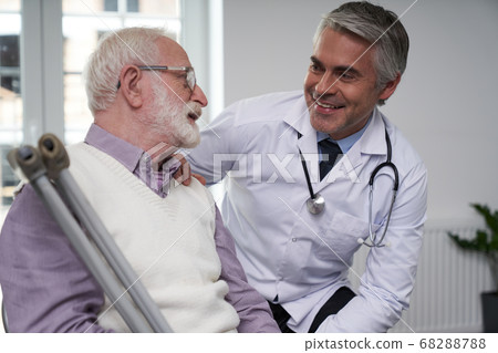 Medical doctor smiling at his eldelry patient with crutches Medical doctor smiling at his eldelry patient with crutches 68288788