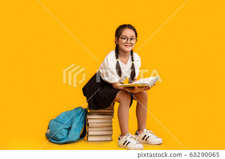 Elementary Student Girl Reading Sitting On Books Stack, Yellow Background Elementary Student Girl Reading Sitting On Books Stack, Yellow Background 68290065