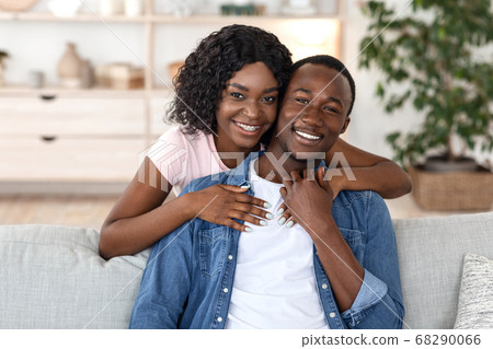 Cheerful african woman hugging her husband from behind Cheerful african woman hugging her husband from behind 68290066