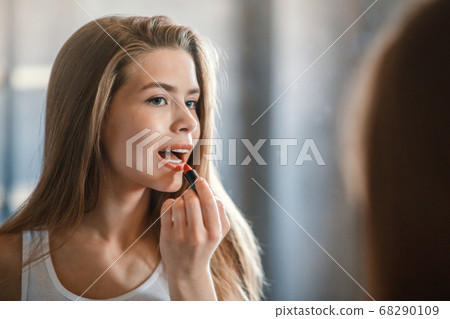 Attractive young lady applying lipstick on her lips near mirror at home, blank space Attractive young lady applying lipstick on her lips near mirror at home, blank space 68290109