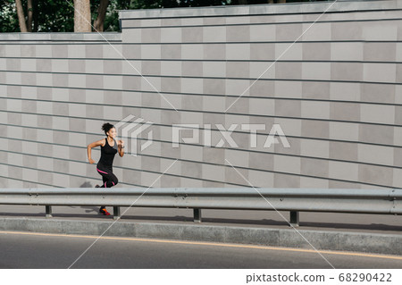 Cross in city at summer. Muscular girl in sportswear with fitness tracker runs along track Cross in city at summer. Muscular girl in sportswear with fitness tracker runs along track 68290422