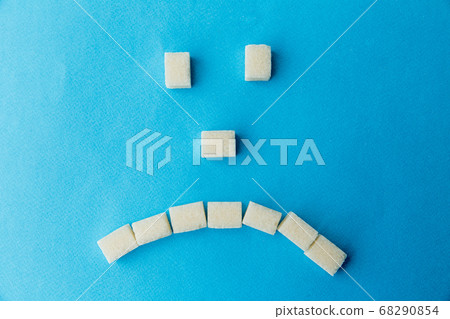 Sad sugar face on the blue table. Sweet food is bad for your teeth. 68290854