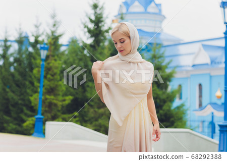 Close-up portrait of young joyous beautiful blonde woman wearing red headscarf and looking somewhere at summer green park. 68292388