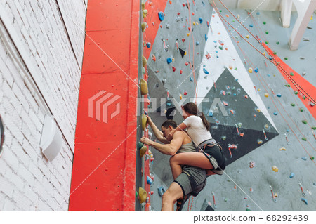 muscular man with a girl training in indoor clymbing gym. 68292439