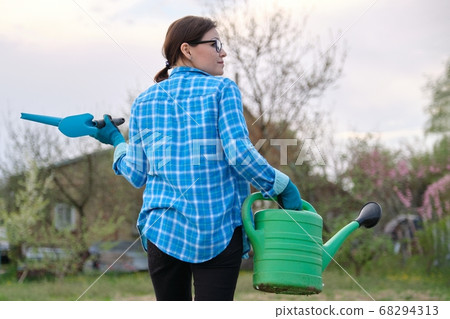 Female gardener holding watering can and garden tools 68294313