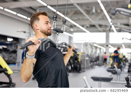 man trains on fitness equipment in the gym, pumps arms muscles, 68295469
