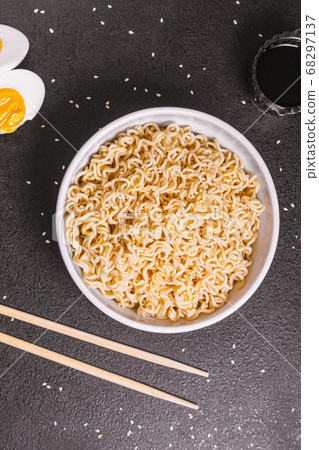 noodles in a plate with sesame seeds and soy sauce, bamboo sticks, boiled eggs on a black table close up. flat ley. copy space 68297137