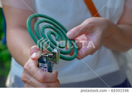 A woman with a mosquito coil is igniting with a lighter in her right hand 68301586