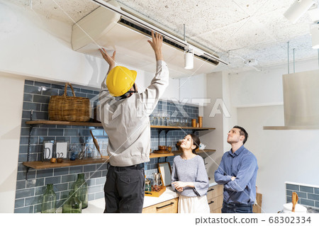 A repairman wearing a yellow helmet and checking the air conditioner A repairman wearing a yellow helmet and checking the air conditioner 68302334