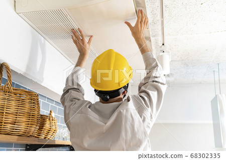 A repairman wearing a yellow helmet and checking the air conditioner A repairman wearing a yellow helmet and checking the air conditioner 68302335