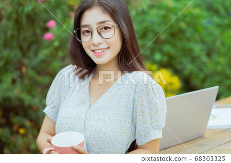 Asian woman holding coffee cup in garden 68303325