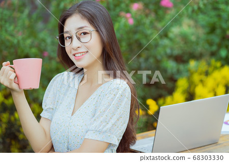 Asian woman holding coffee cup in garden 68303330