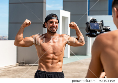 Happy muscular Hispanic man fitness vlogger flexing his arm muscles while recording  68303496