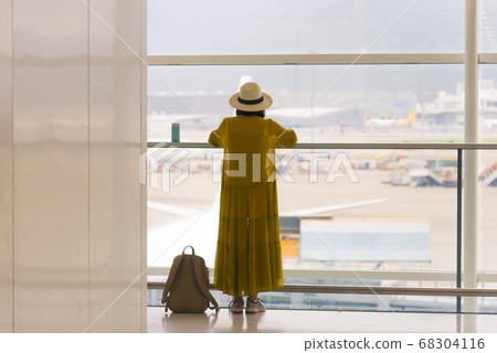 Back view of traveling girl standing near window at the international airport terminal Back view of traveling girl standing near window at the international airport terminal 68304116