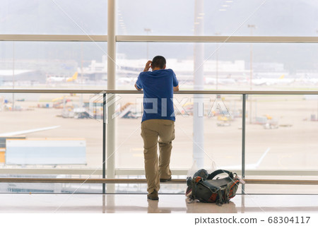 Back view of traveling man standing near window at the international airport terminal Back view of traveling man standing near window at the international airport terminal 68304117