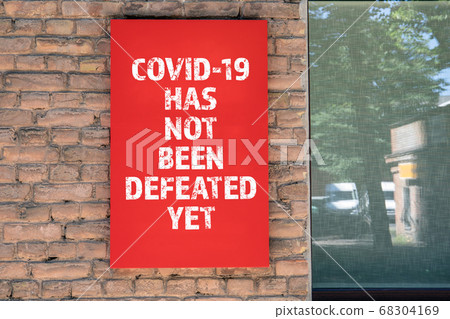 COVID-19 HAS NOT BEEN DEFEATED YET. Red advertising sign on the masonry wall COVID-19 HAS NOT BEEN DEFEATED YET. Red advertising sign on the masonry wall 68304169