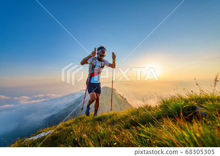 Man with poles in the mountains with sunset behind Man with poles in the mountains with sunset behind 68305305