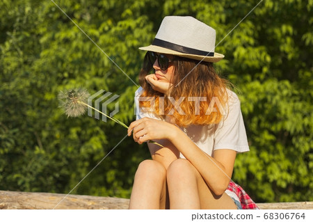 Sad girl sitting in nature with a fluffy dandelion, serious unhappy teenager Sad girl sitting in nature with a fluffy dandelion, serious unhappy teenager 68306764