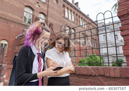 Female student walking and talking with woman teacher, girl showing on smartphone screen Female student walking and talking with woman teacher, girl showing on smartphone screen 68307587