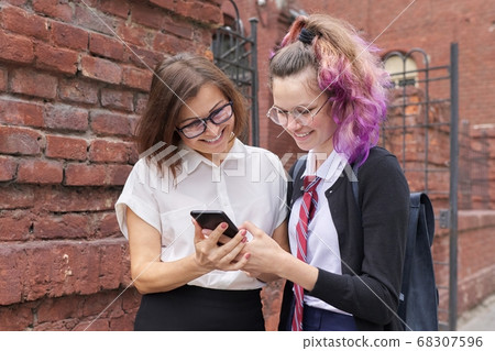 Female student walking and talking with woman teacher, girl showing on smartphone screen Female student walking and talking with woman teacher, girl showing on smartphone screen 68307596