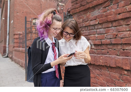 Female student walking and talking with woman teacher, girl showing on smartphone screen Female student walking and talking with woman teacher, girl showing on smartphone screen 68307600