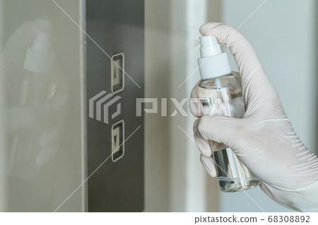 Closeup Asian woman hand wearing medical gloves and spraying Anti-Bacterial Sanitizer Spray to the elevator button before cleaning press, Coronavirus Network Outbreak, health care and cleaning covid19. 68308892